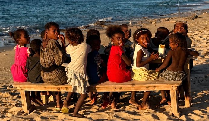 Des enfants assis sur des bancs autour d'une table, sur la plage
