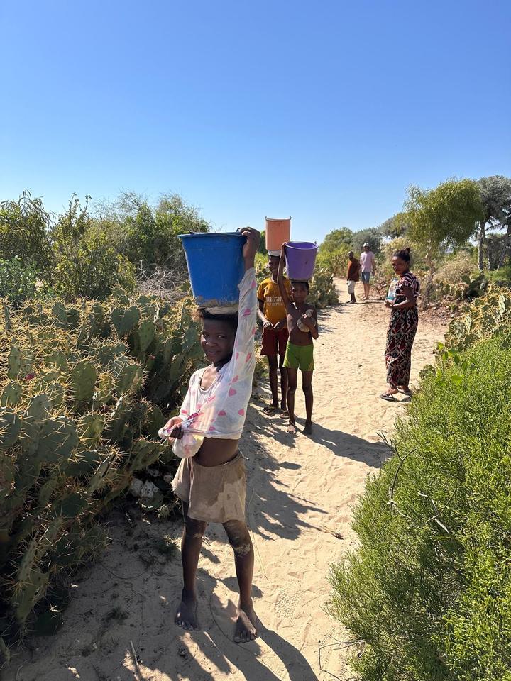 Des enfants portent des seaux d'eau sur la tête le long d'un chemin de sable