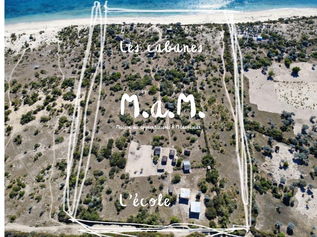 Vue aérienne du terrain de M.a.M. : les cabanes près de la plage et l'école au milieu de la brousse